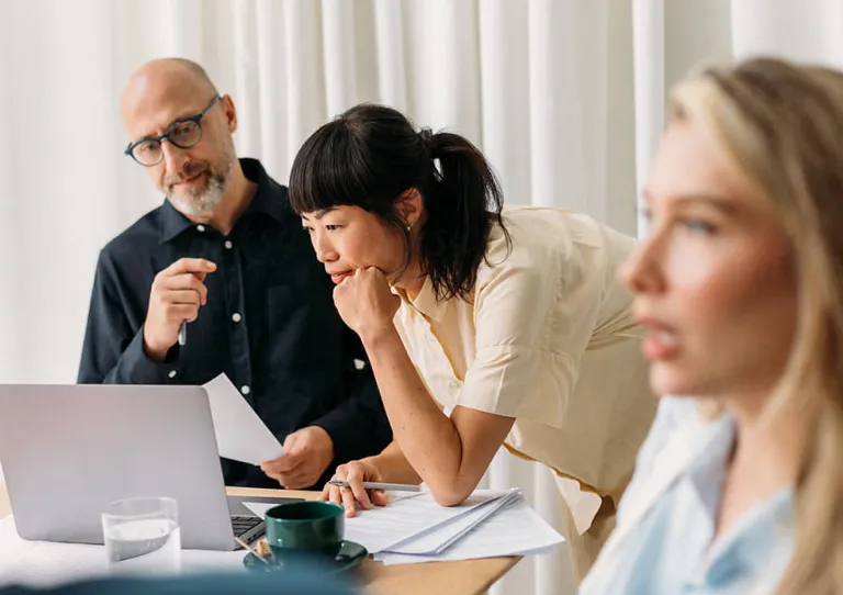 Two people in background reviewing laptop one person speaking in forground